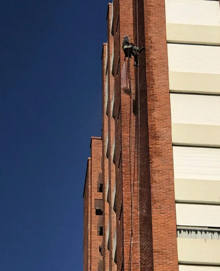 Operario de Alta Group suspendido con arnés de seguridad sobre una pared de ladrillo a la vista